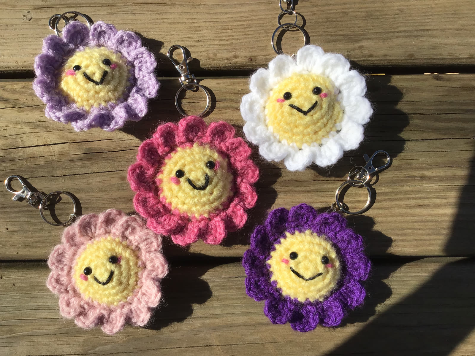 Five smiling crocheted flower keychains in purple, pink, and white
