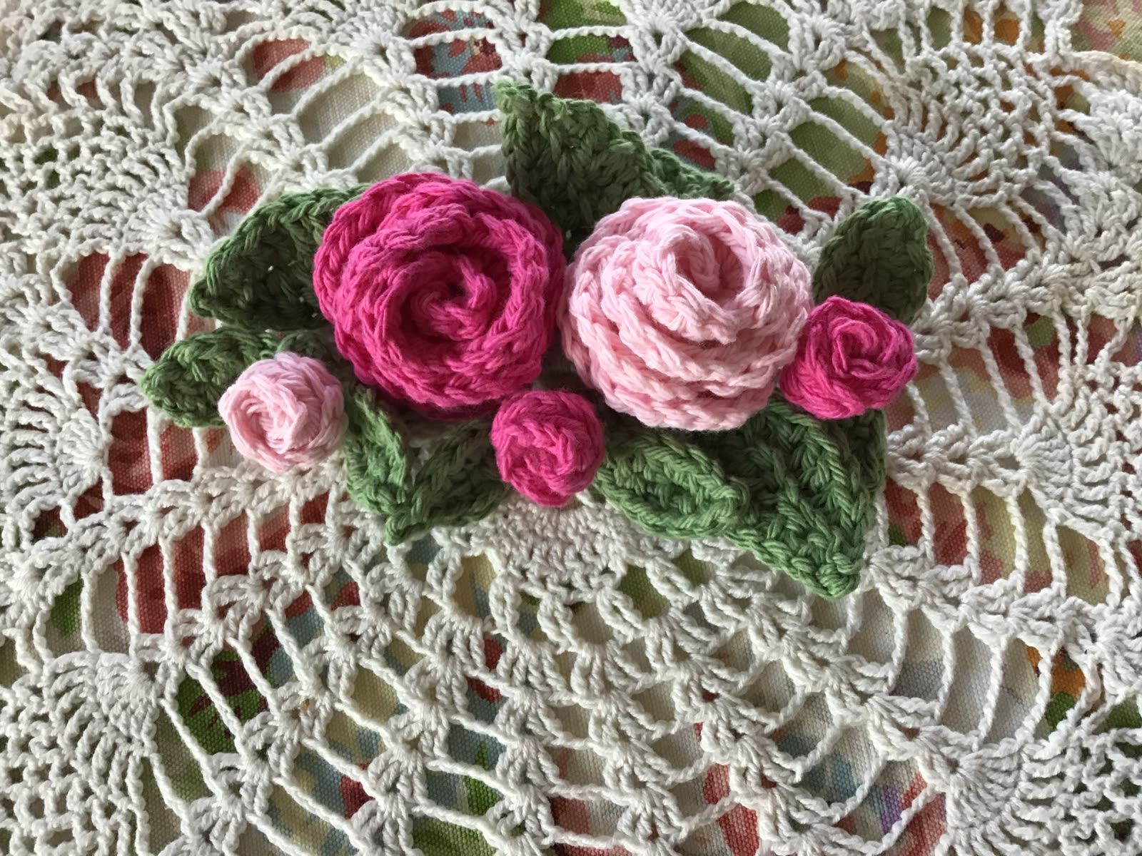 Pink crocheted roses and rosebuds arranged with green leaves